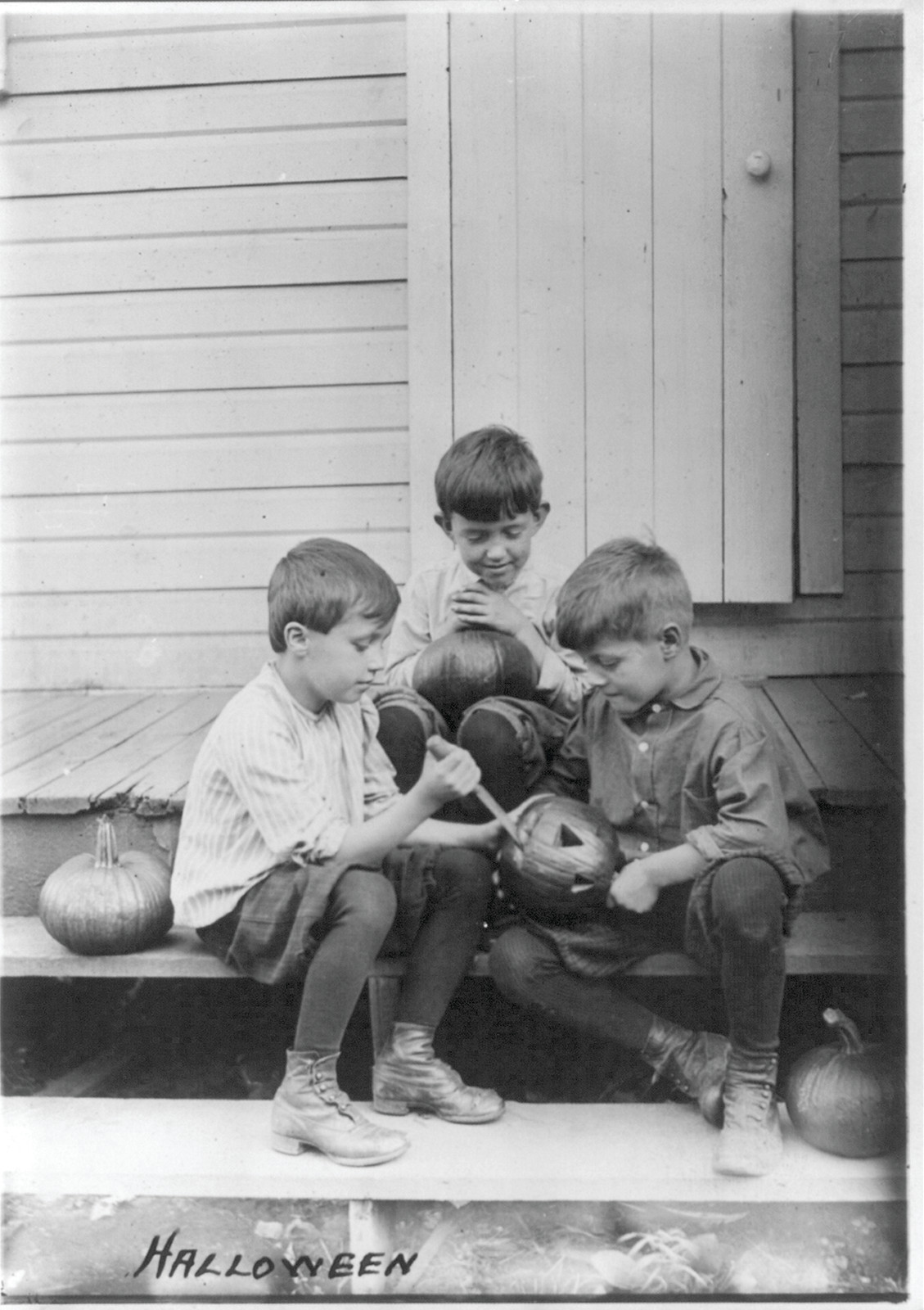 Halloween: three boys carving jack-o'-lanterns on the porch steps, c. 1917 — historic photograph