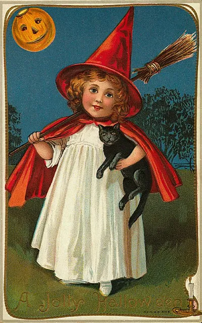 A girl in a witch hat and red cape holding a black cat