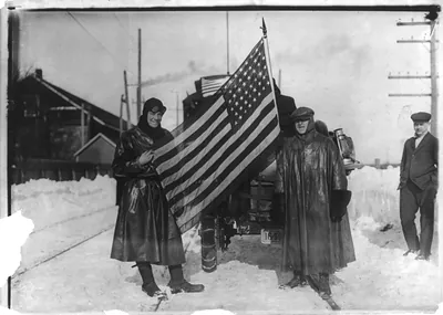 New York-to-Paris automobile race: [Two men holding U.S. flag behind automobile]