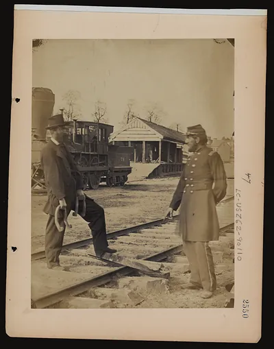Two men on railroad tracks beside a locomotive and depot