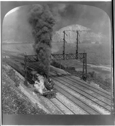 Steam locomotive with smoke passing signal gantries beside a rocky cliff
