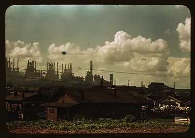 Steel mill smokestacks rising behind rows of houses
