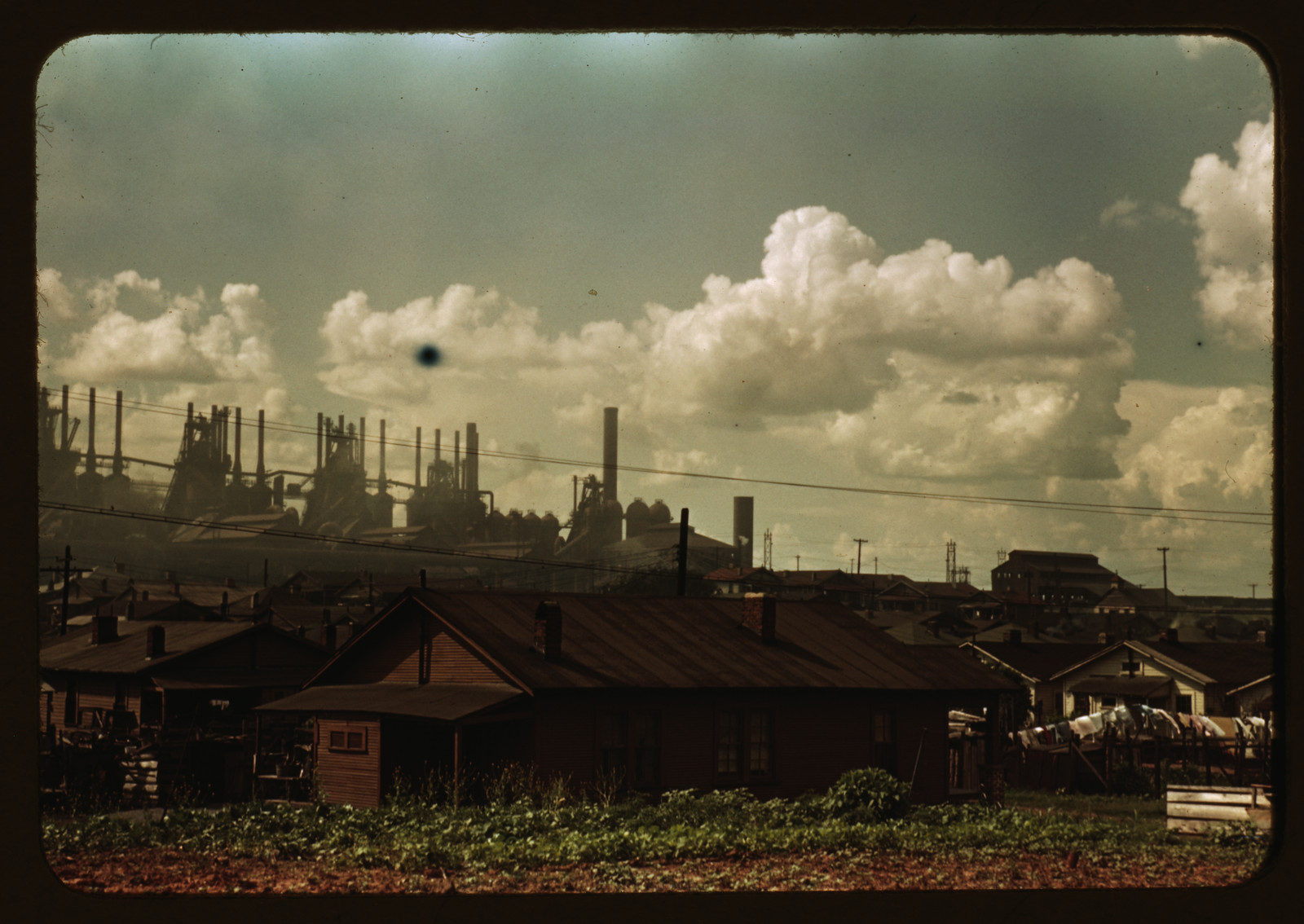 Steel mill smokestacks rising behind rows of houses — historic image
