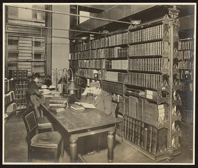 Two readers at a long table beside tall bookshelves