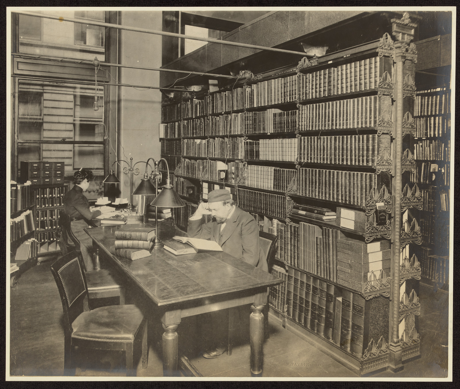 Two readers at a long table beside tall bookshelves — historic image