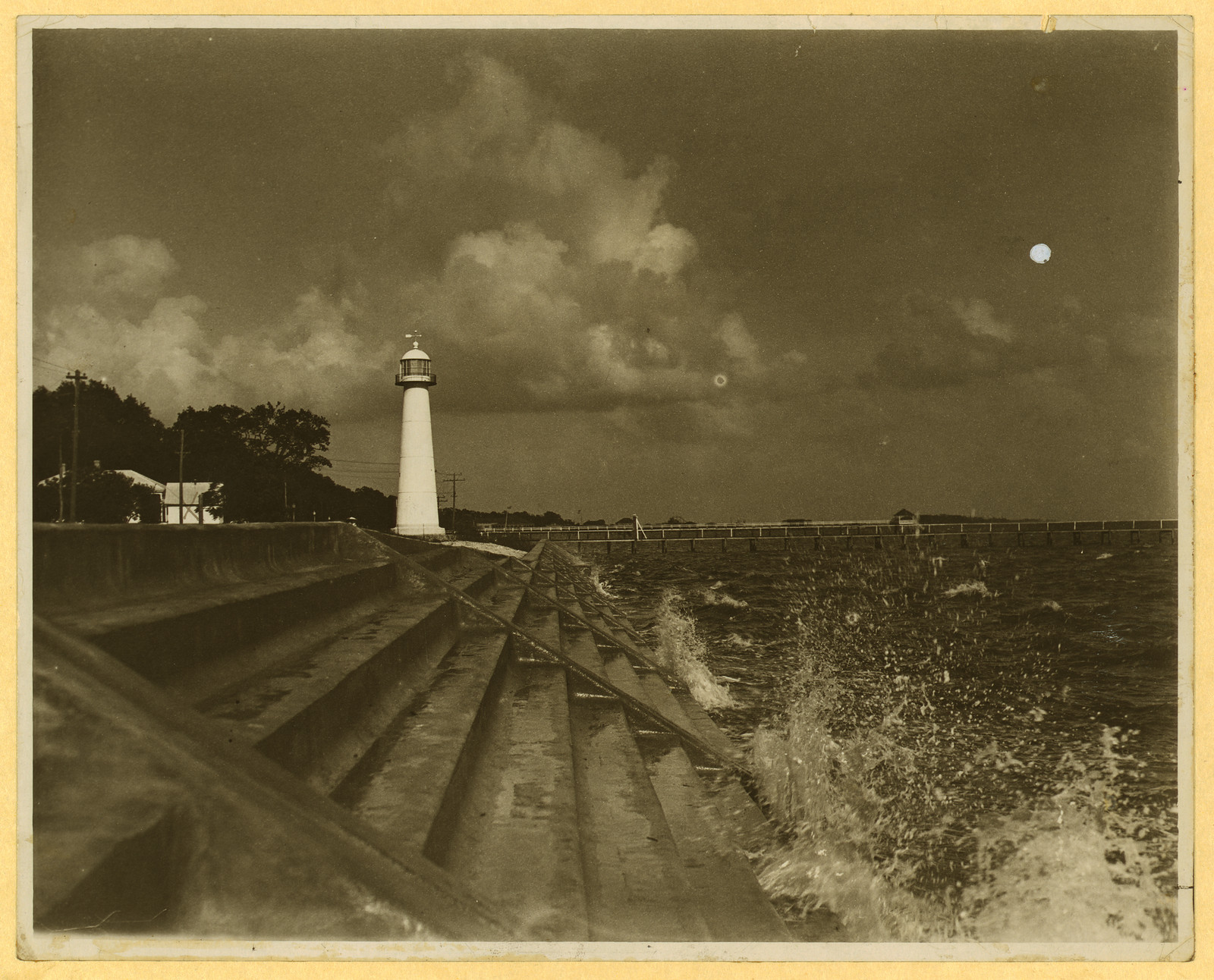 White lighthouse above stepped seawall, waves breaking, sepia photograph — historic photograph