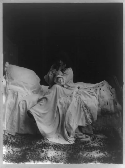 [Sarah Bernhardt as Camille, full-length portrait, seated on bed, facing slightly left, head resting on hands]