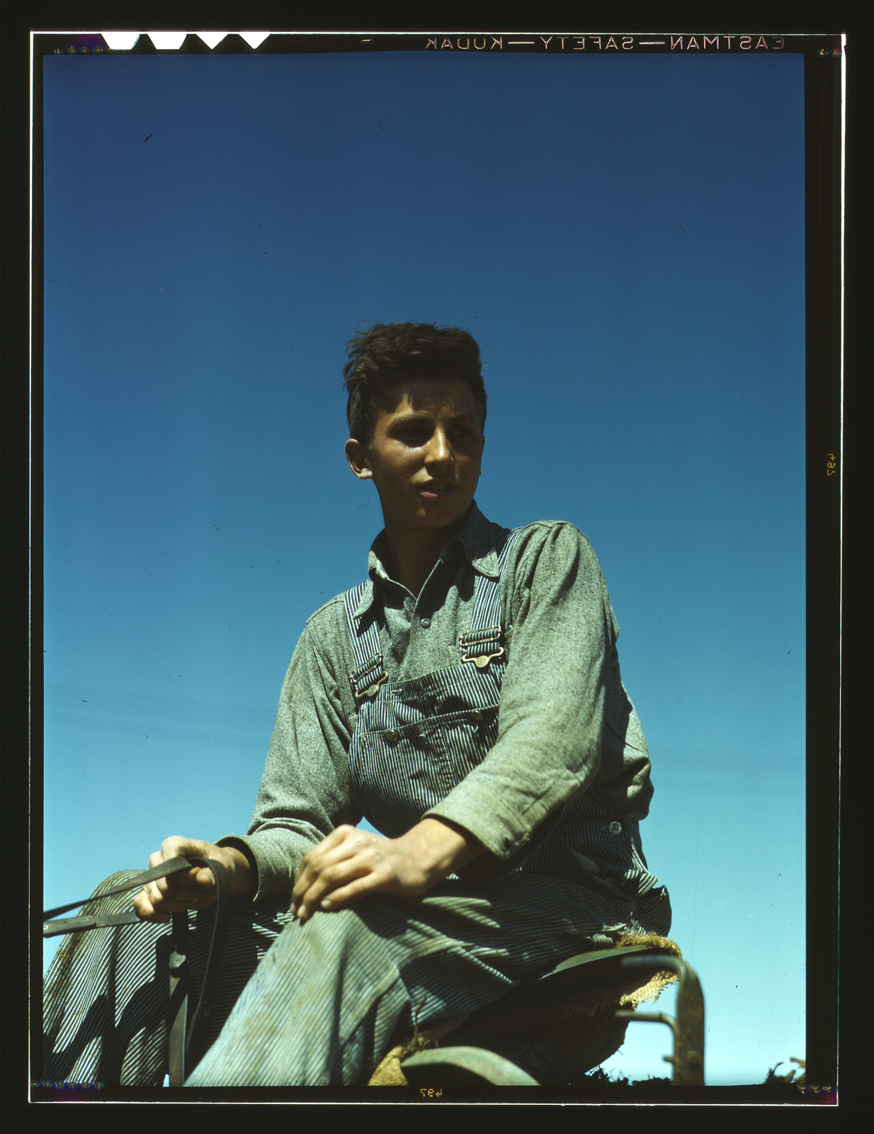 Portrait of a farm boy in overalls on farm machinery — historic image