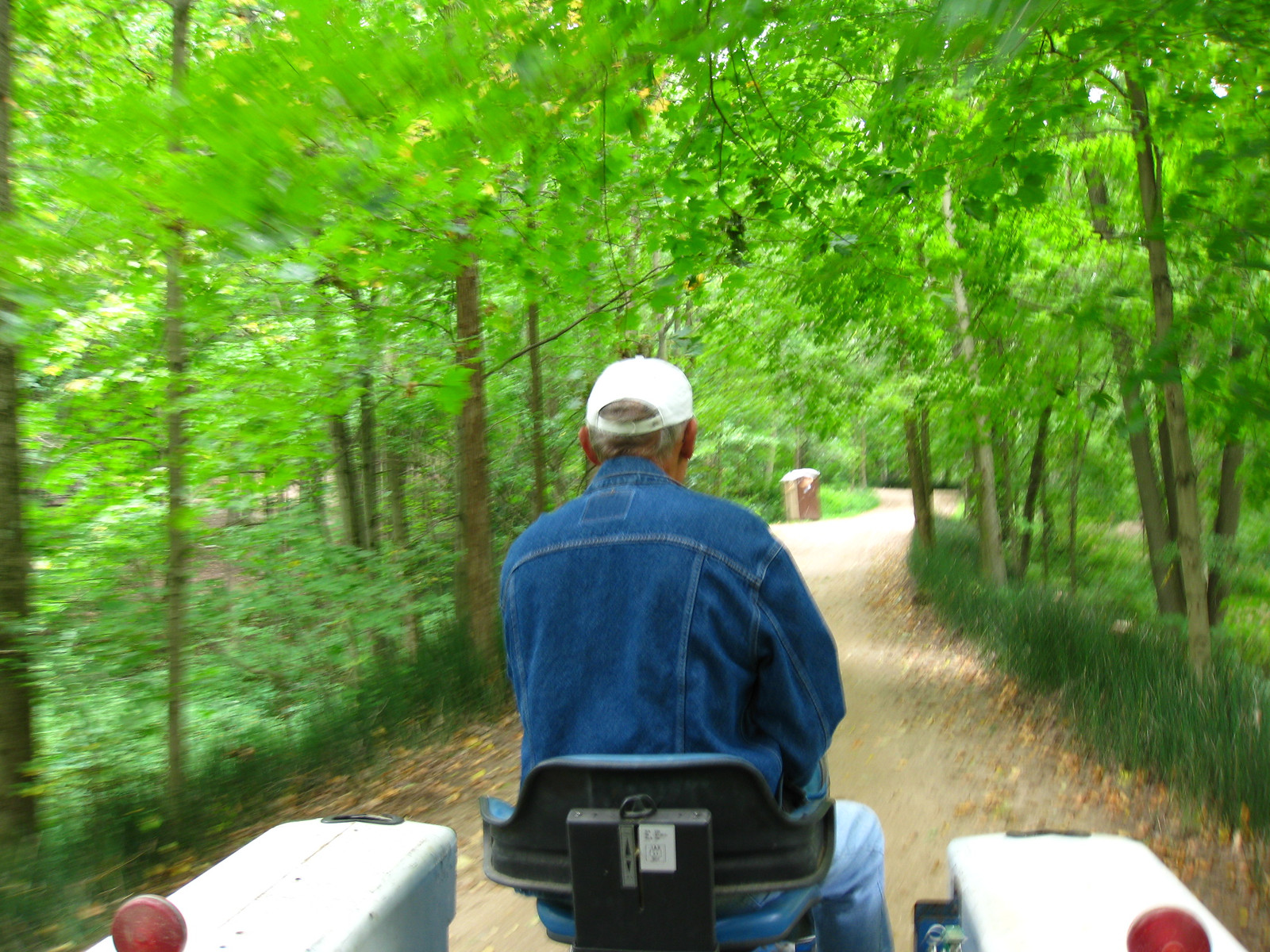 Man in denim jacket and cap driving a vehicle on a woodland path — historic image