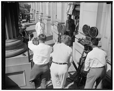 Newsreel cameramen filming officials on a stone balcony