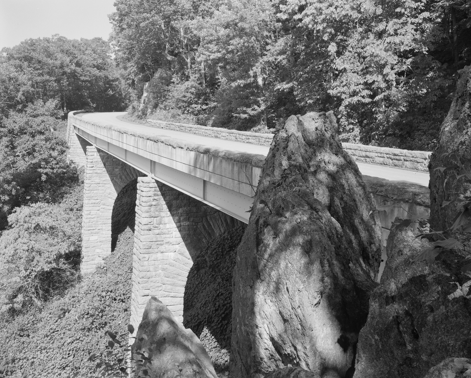 Stone-faced bridge over rock outcrops, wooded gorge, black and white photograph — historic photograph
