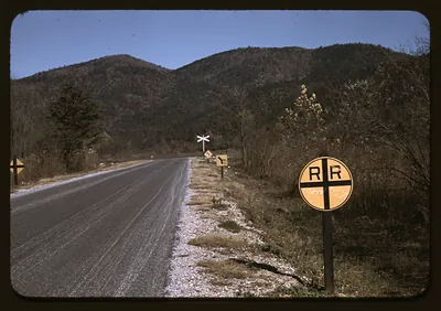 Paved mountain road with railroad crossing signs and wooded hills