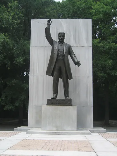 Bronze statue of Roosevelt with raised arm before granite wall