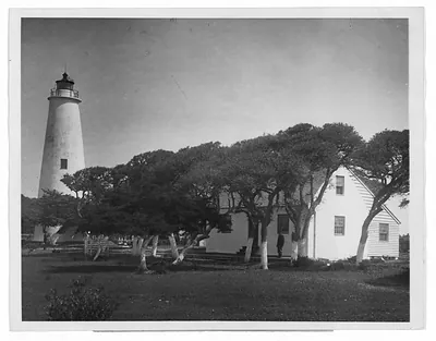 White lighthouse beside a keeper's house and windswept trees
