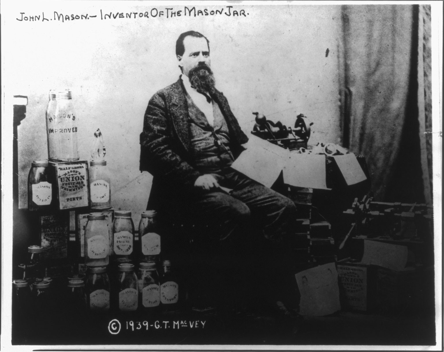 [John Landis Mason, full-length portrait, seated, facing right, alongside stack of Mason jars] — historic photograph