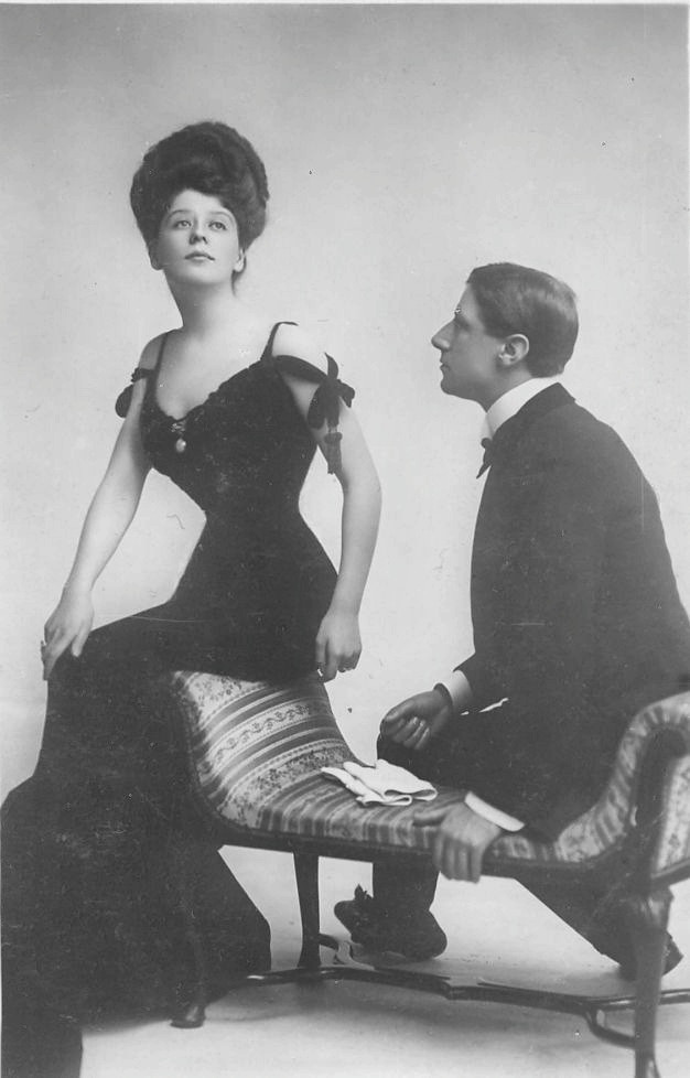 Woman in dark corset dress with seated man, early 1900s studio portrait — historic image