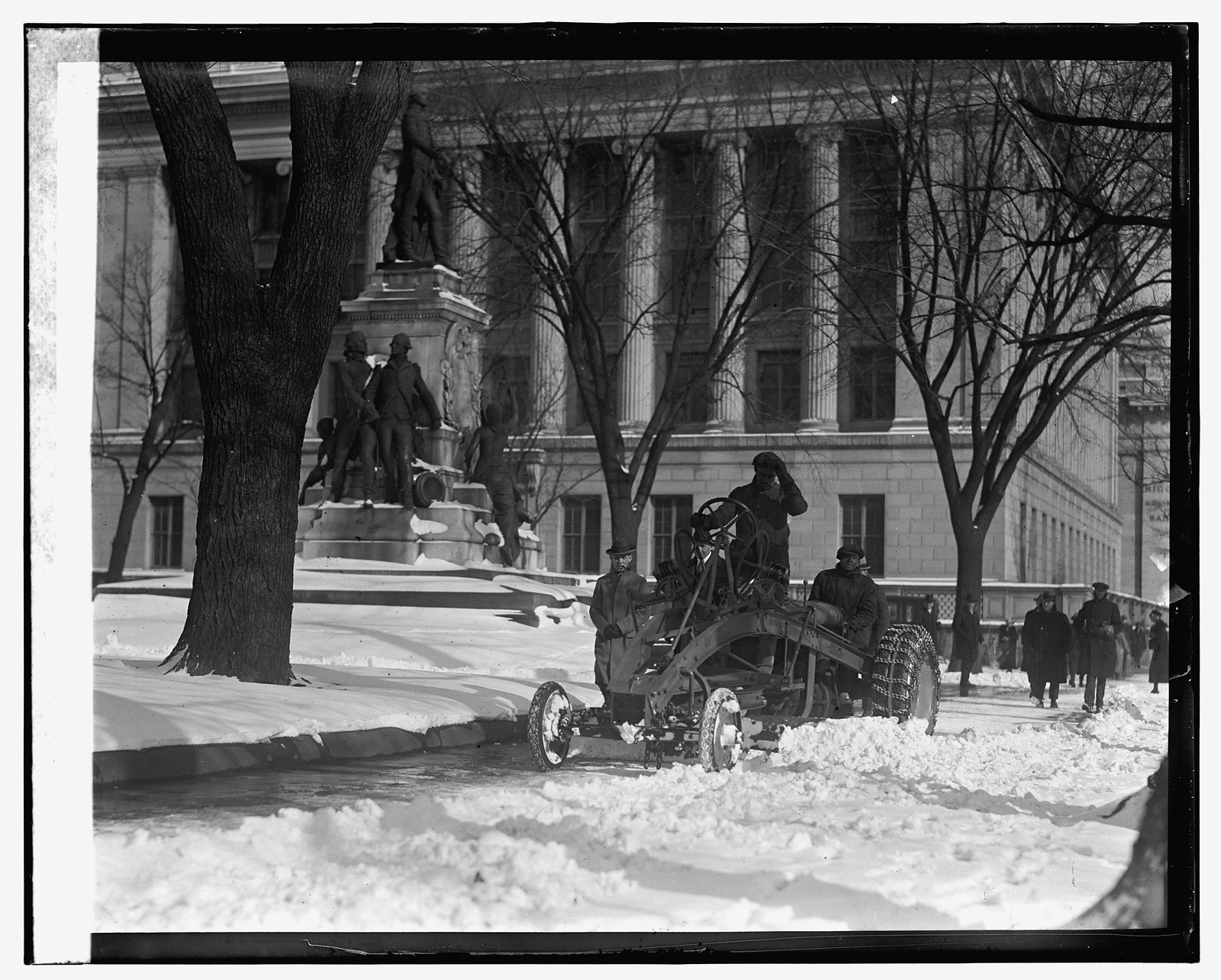 Men clearing deep snow with a machine beside a monument — historic image