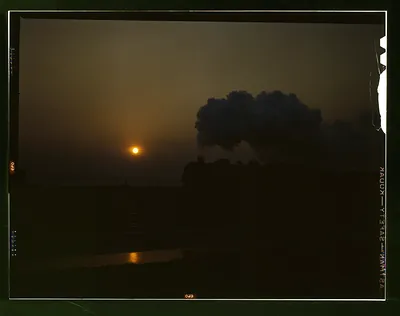 Steam locomotive silhouetted at sunset with smoke plume