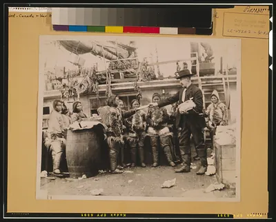 [Robert Edwin Peary, full-length portrait, standing on deck of ship or dock, facing left, distributing gifts to Eskimos, Greenland]