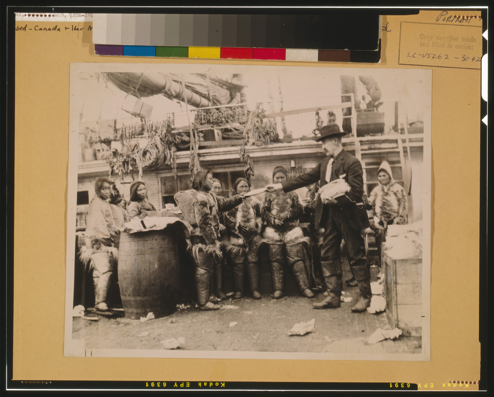[Robert Edwin Peary, full-length portrait, standing on deck of ship or dock, facing left, distributing gifts to Eskimos, Greenland], [between 1886 and 1909] — historic photograph