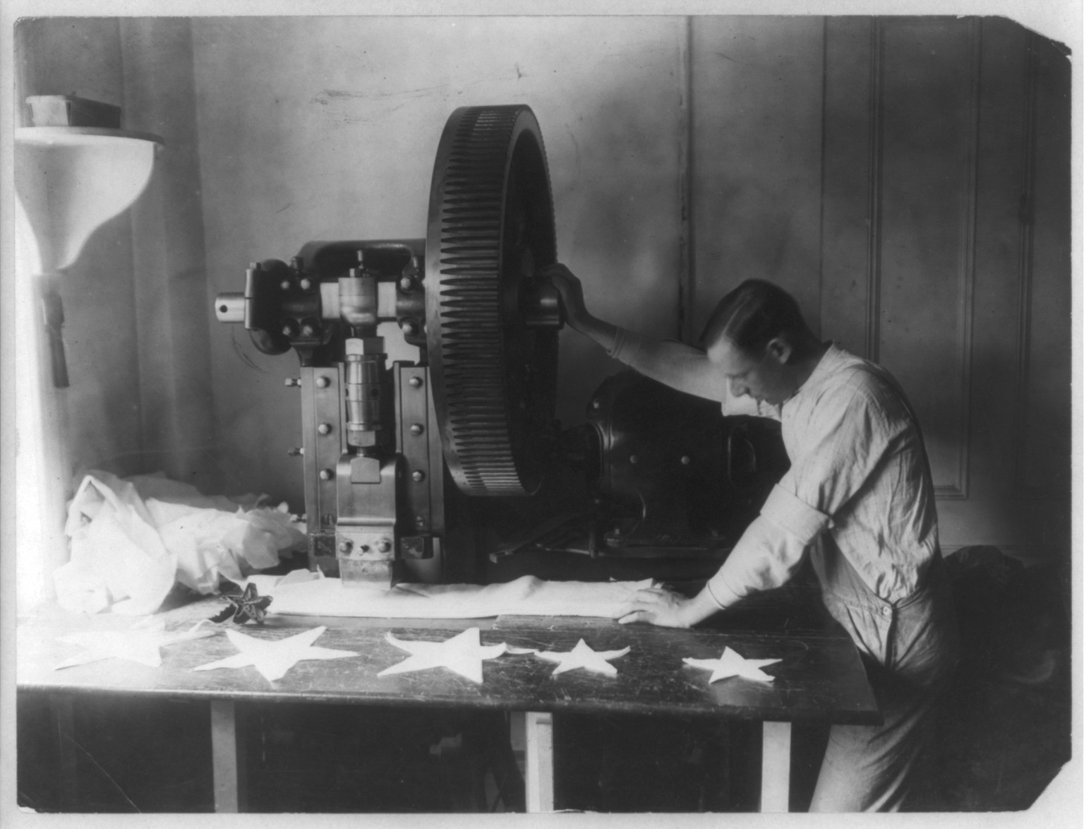 [Flag making - man cutting out stars with machine], [190-] — historic photograph