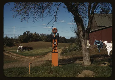 [Gas pump with clothesline, barn and horse-drawn wagon in background]