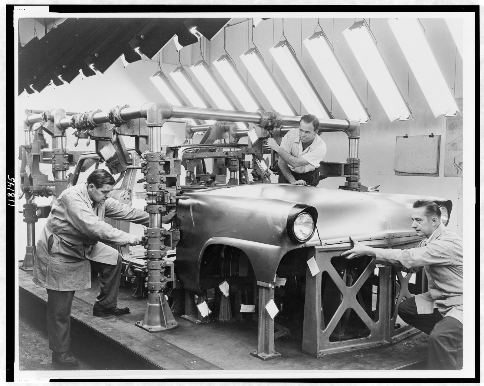 [Three men working on a Ford automobile on assembly line], 1954 — historic photograph
