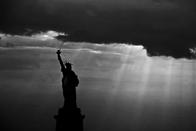 Statue of Liberty silhouetted against dark clouds with light rays