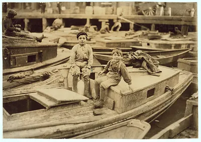 Two boys sitting on wooden boats in a boatyard