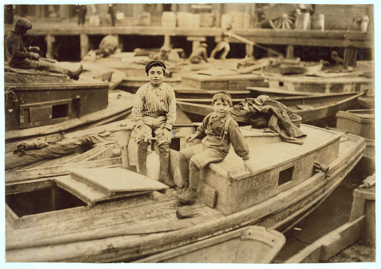 Two boys sitting on wooden boats in a boatyard — historic image