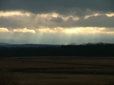 Sunbeams breaking through clouds over a wooded rural landscape