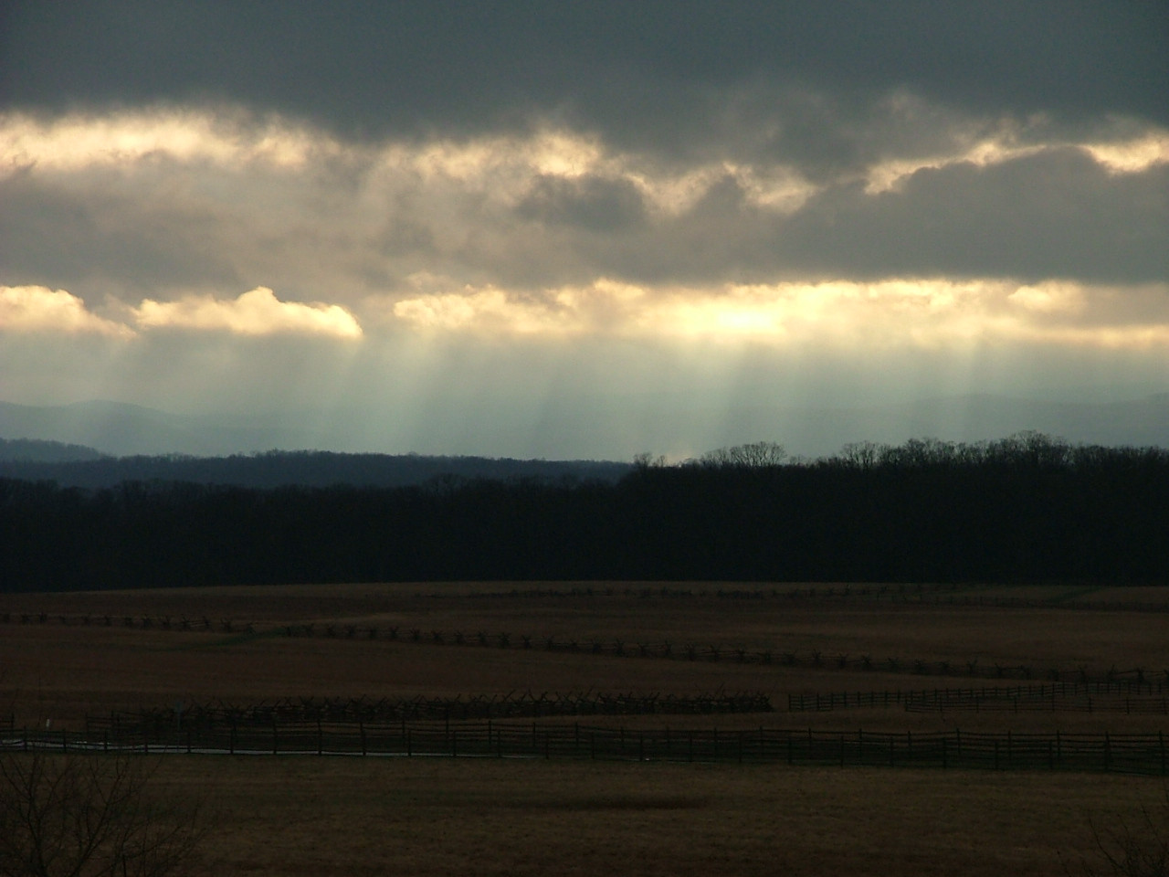 Sunbeams breaking through clouds over a wooded rural landscape — historic image