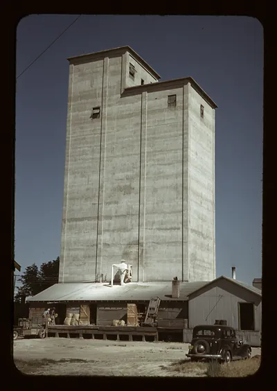 Concrete grain elevator with warehouse and parked vintage car