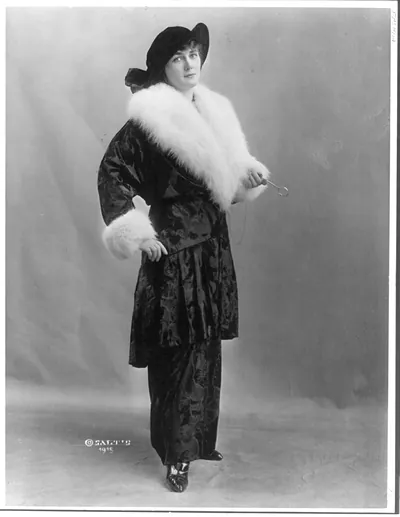 [Woman modeling evening suit with long, fur-trimmed coat]