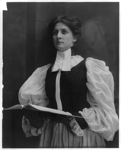 [Young woman modeling: half lgth., standing in choir robe, holding open music book]
