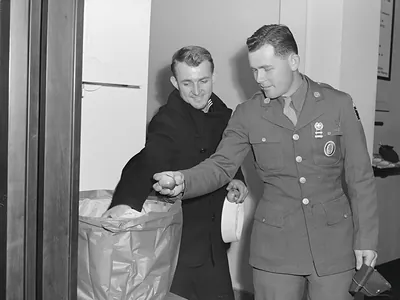 Two servicemen in uniform, one passing an apple