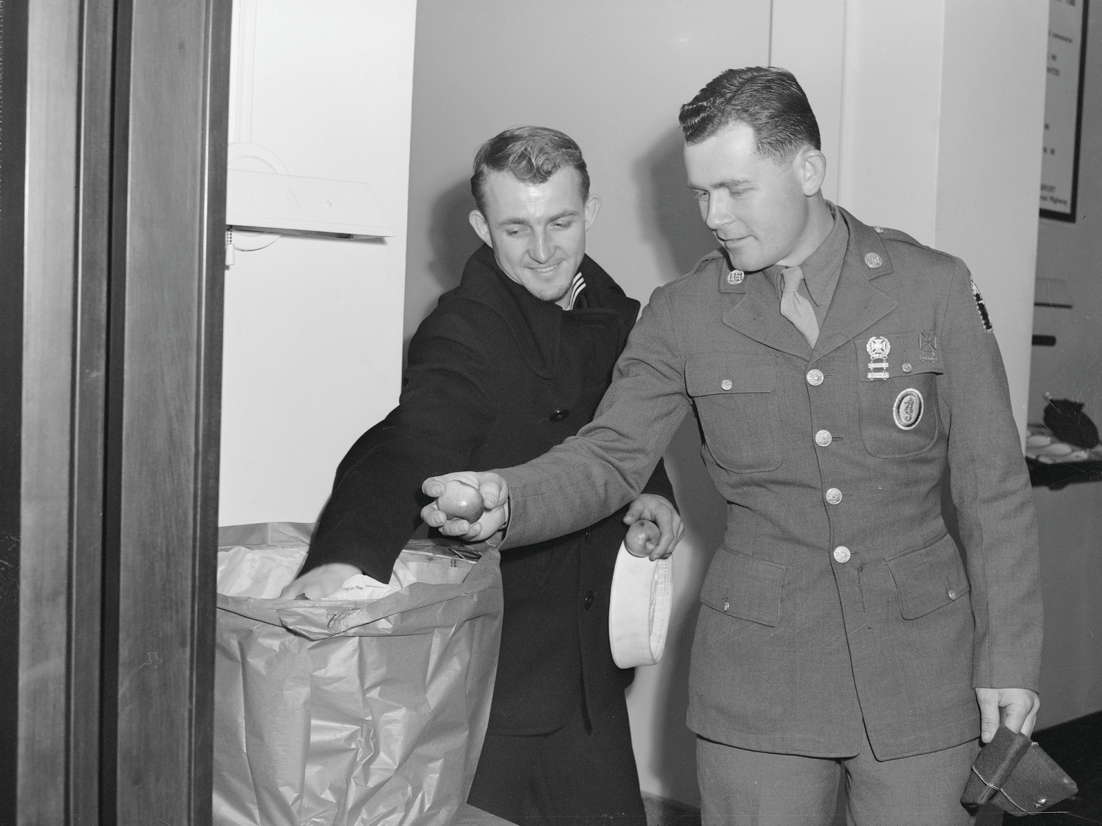 Two servicemen in uniform, one passing an apple — historic image