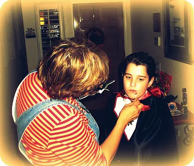 Woman applying vampire makeup to a boy in a cape