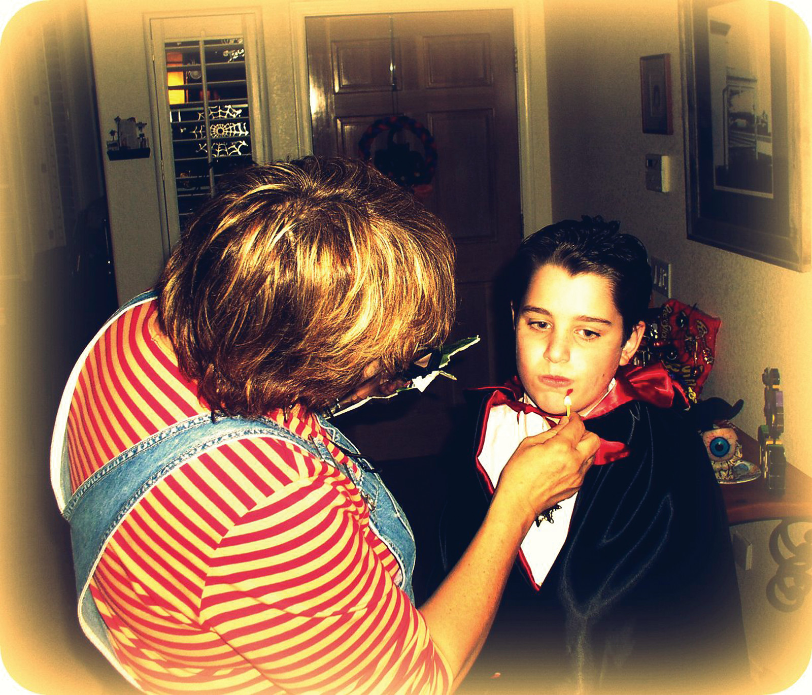 Woman applying vampire makeup to a boy in a cape — historic image