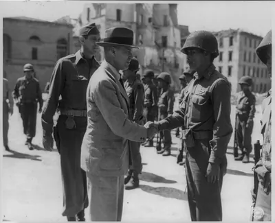 Under Sec'y of War, Robert Patterson, congratulating Lt. Masand Otake, Lahaina, Mauith, Hawaii, 100th Inf. Bn., an American of Japanese descent on the outstanding job done by the Battalion. Lt. Gen. Mark W. Clark [and others], C.G. Fifth army, stands behind them. Fifth Army, Leghorn Area, Italy