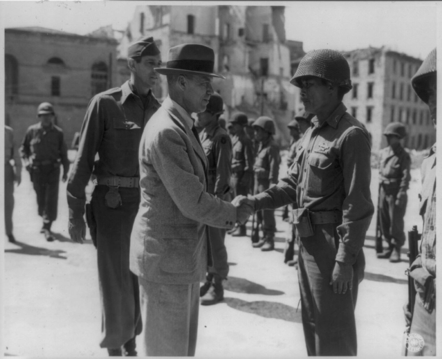 Under Sec'y of War, Robert Patterson, congratulating Lt. Masand Otake, Lahaina, Mauith, Hawaii, 100th Inf. Bn., an American of Japanese descent on the outstanding job done by the Battalion. Lt. Gen. Mark W. Clark [and others], C.G. Fifth army, stands behind them. Fifth Army, Leghorn Area, Italy — historic photograph
