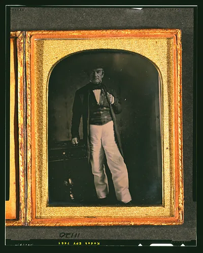 [John Ross, full length portrait, facing front standing next to a small table]