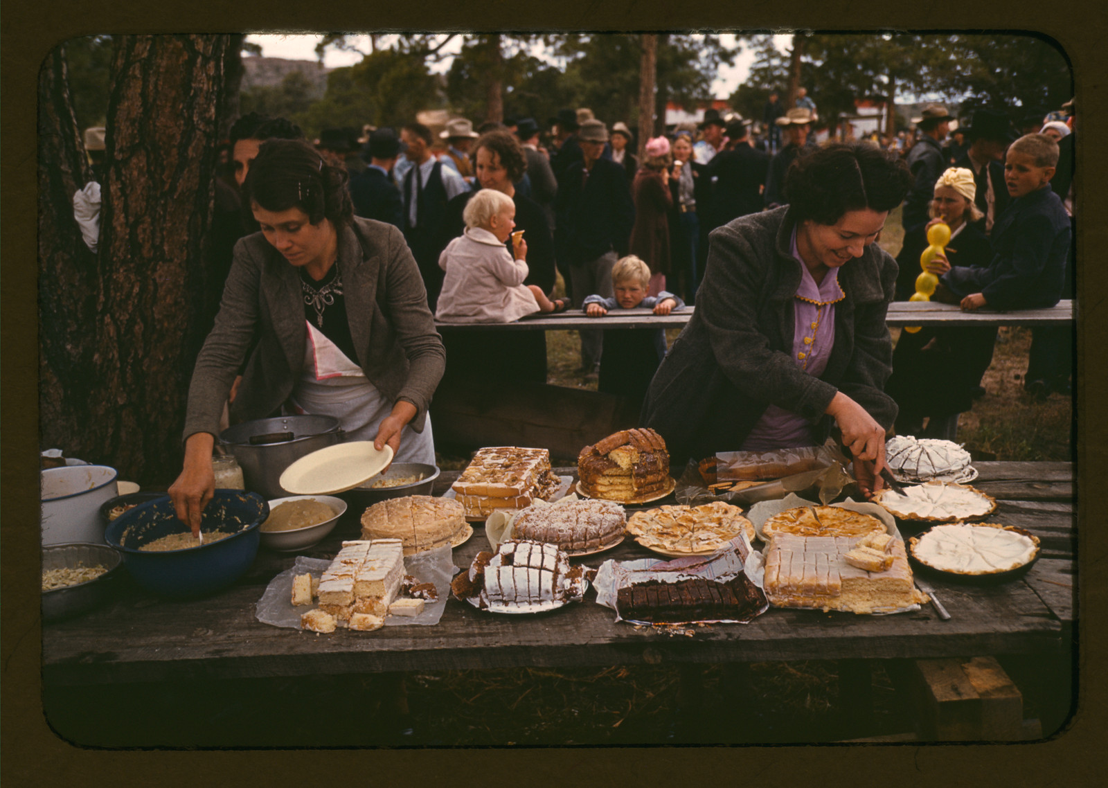 Women serving pies and cakes at an outdoor food table — historic image