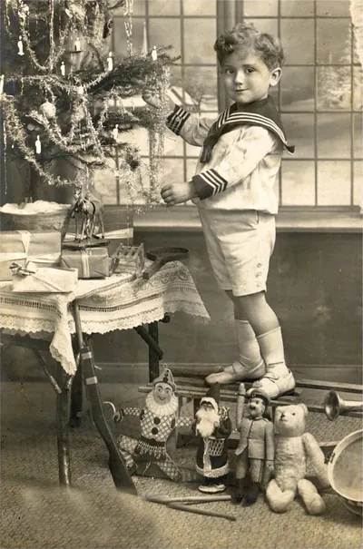 Boy decorating a Christmas tree beside toys