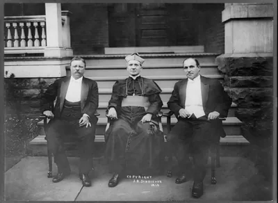 [Theodore Roosevelt, Rev. M.J. Hoben, and John Mitchell, posed, seated in front of porch]