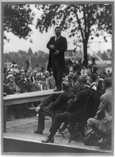 [Theodore Roosevelt standing on table outdoors and making speech to men seated around him, hands at waist] / Smith Art Photography, Freeport, Ill.