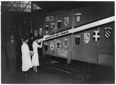[Woman ceremoniously painting decoration on French Gratitude Train which toured U.S. in 1948-49; side of boxcar is decorated with French Provincial Crests]