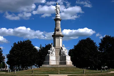 Stone monument with statues on grassy hill under blue sky