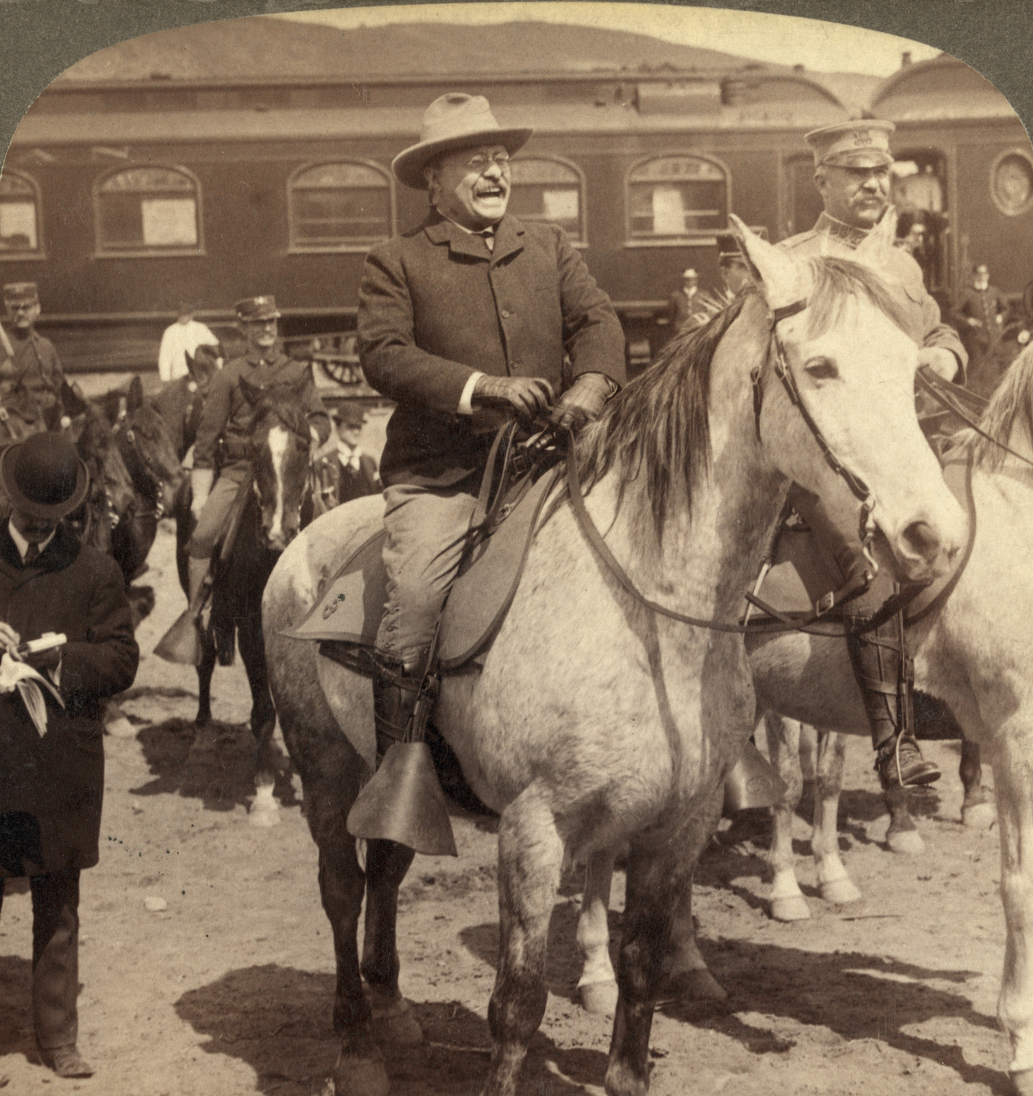 Laughing rider on gray horse beside railway car — historic image
