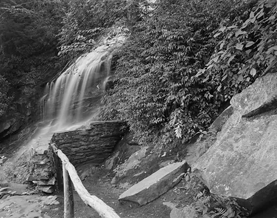 Waterfall over stone ledge beside log railing